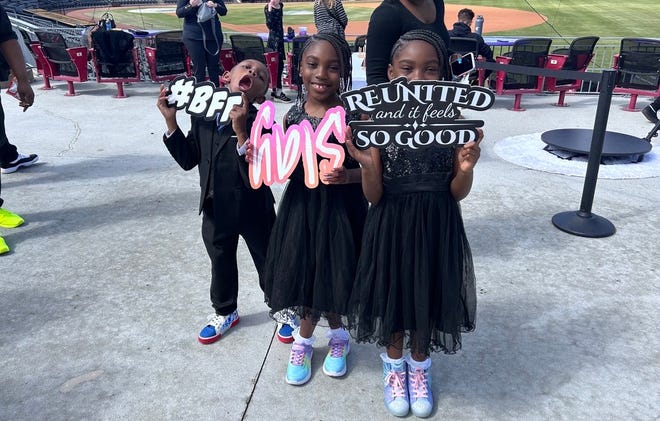 From left: Manny Baker, 6, with twin sisters Harmony Baker, 8, and Symphony Baker, 8, posing with signs at the 3rd annual It's a Family Affair Sneaker Ball event at Segra Stadium, Mar. 2, 2024.