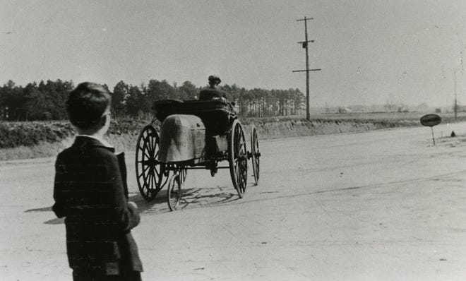 Photo of a 1900 "Holsman" as it stopped in Fayetteville to get gas on it's way north in the late 1930s as submitted by Norwood Bryan Sr. The driver is unidentified by Dennis Deese is to the left. The station he stopped was on Raeford Road. It was said that the man had come from the West Coast.
